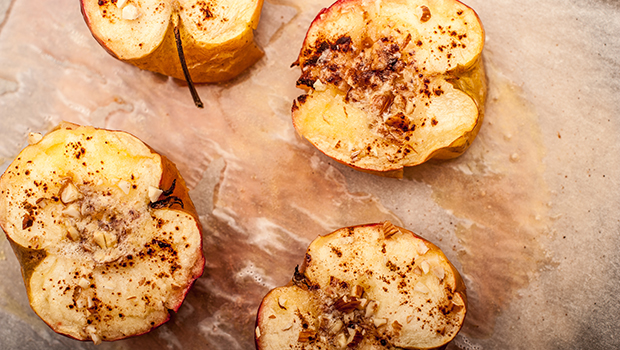 Baked apples slices in half with cinnamon sprinkled on top, all on a wooden table
