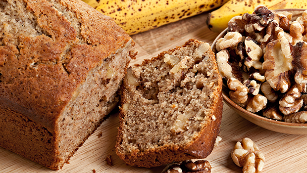 Slice of banana bread with a ripe whole banana and small bowl of walnuts on the side
