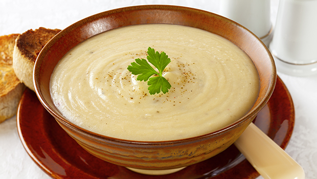 Cauliflower potato soup in a brown ceramic bowl with a garnish