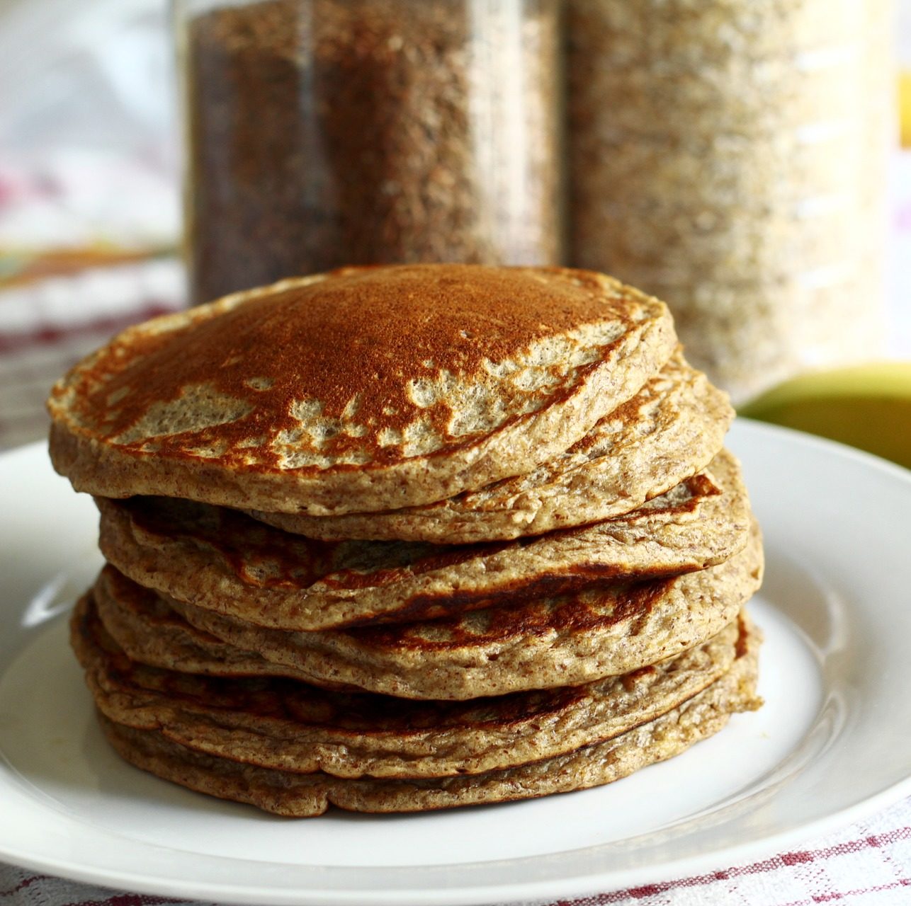 Stack of six cooked brown pancakes on a white round plate