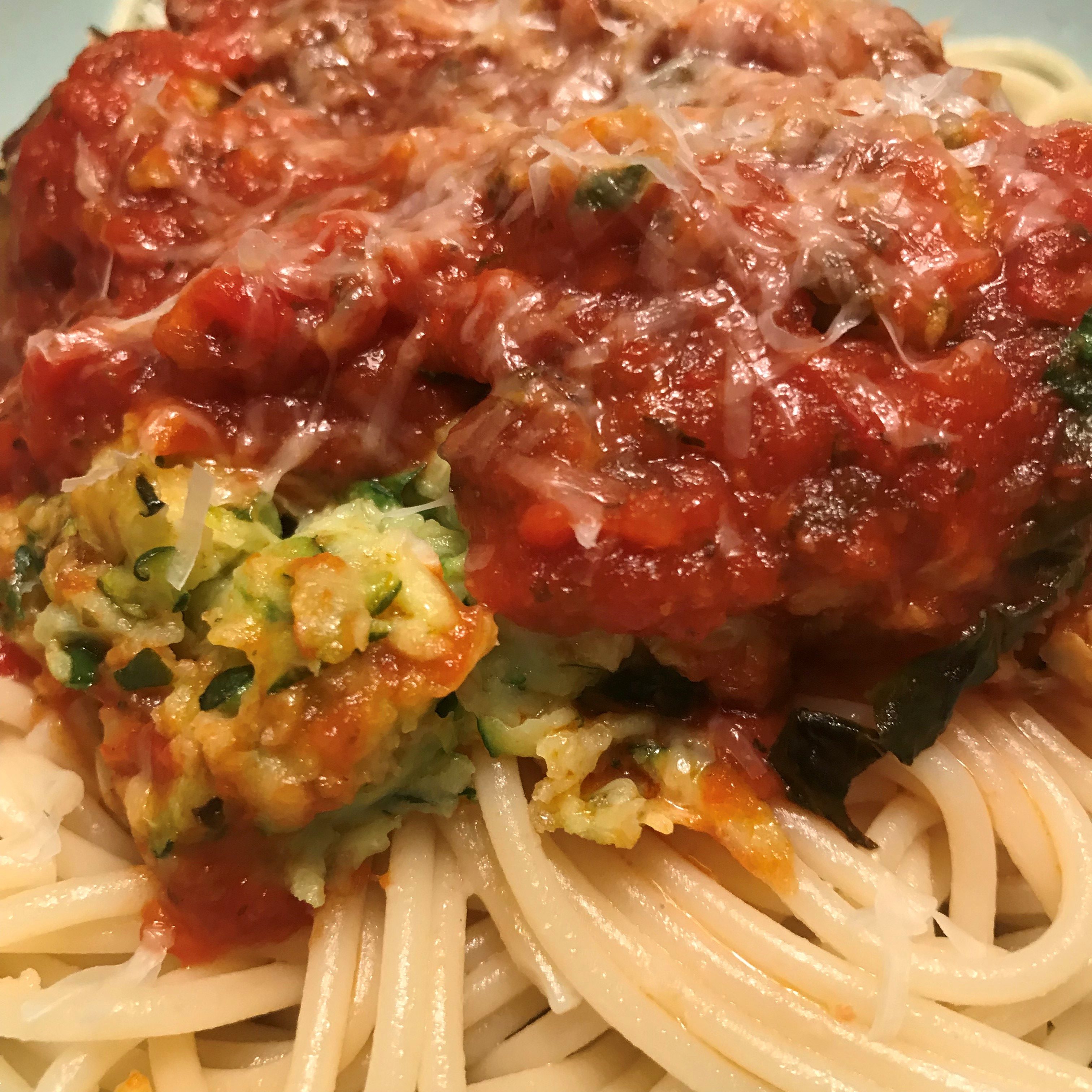 Close-up view of zucchini meatballs, a red sauce, on top of spaghetti noodles
